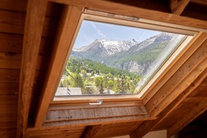 Une lucarne offrant une vue sur un paysage montagneux, avec des poutres en bois et un ciel dégagé.