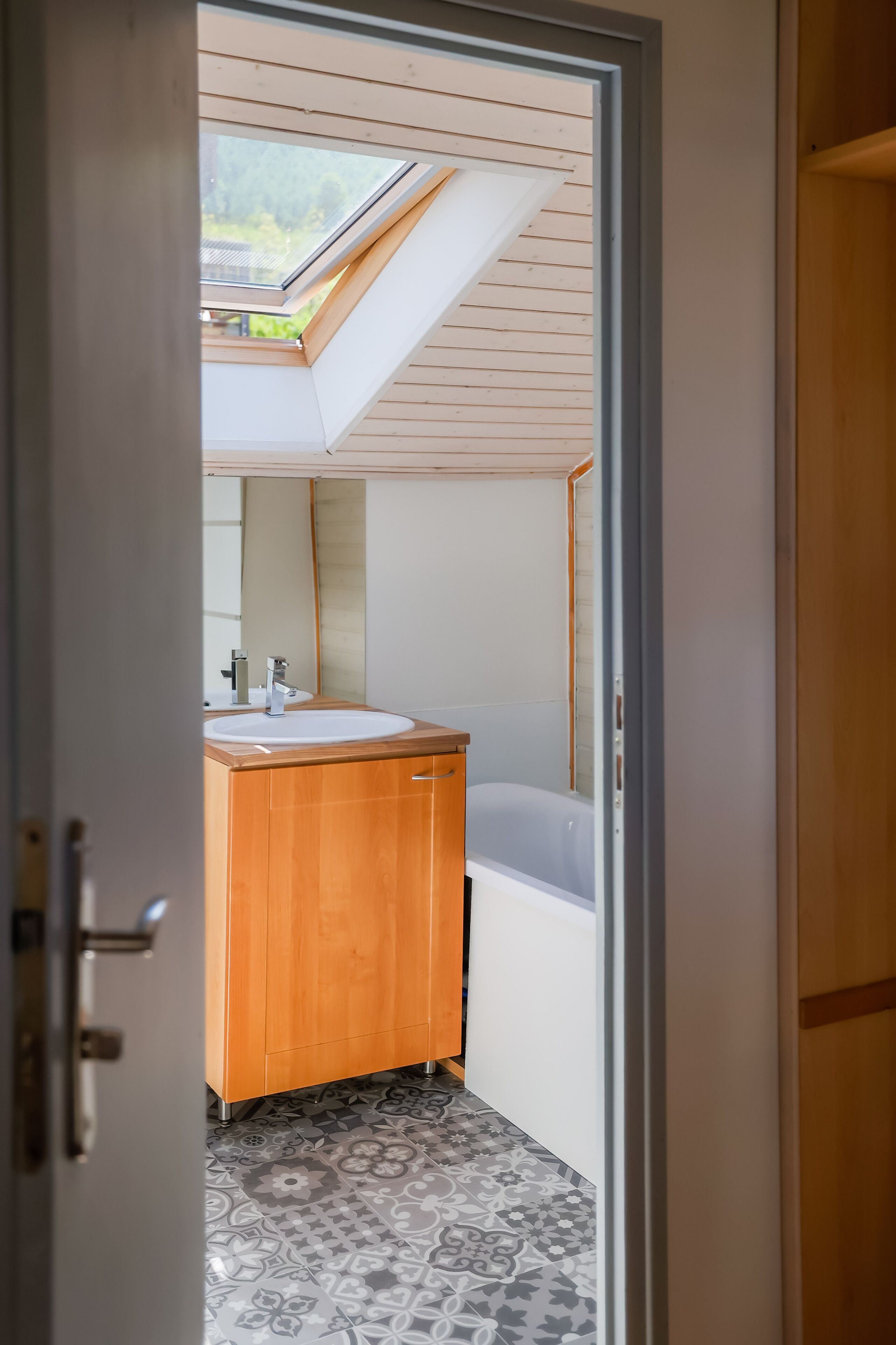 Ein kleines Badezimmer mit Dachfenster, Holzschränken und einer Badewanne.