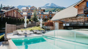 A pool area with lounge chairs, a wooden building with balconies, and a mountain backdrop. - Résidence Sunêlia Les Logis d'Orres (Les Orres)
