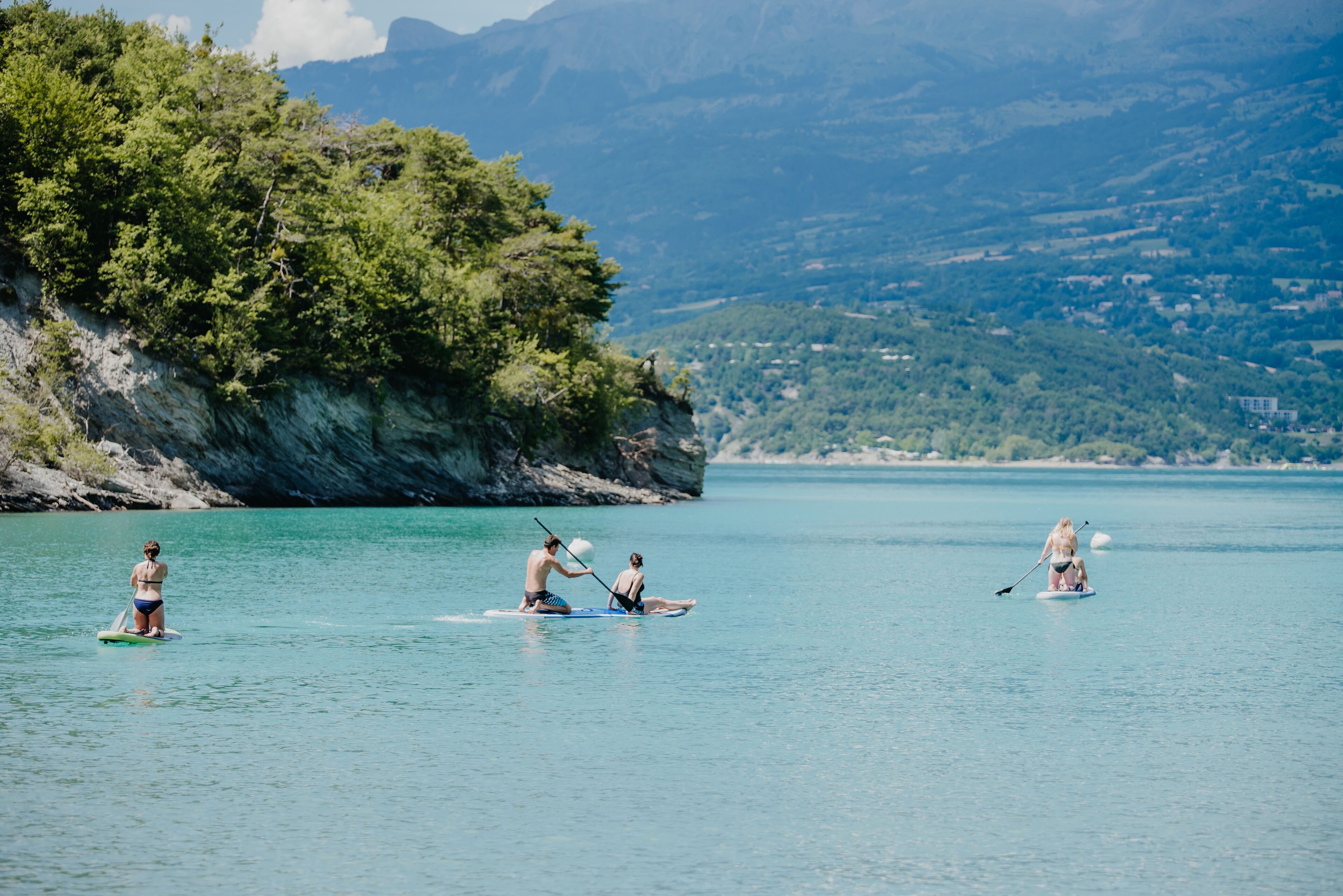A group of people paddleboarding on a calm body of water with a mountainous landscape in the background.