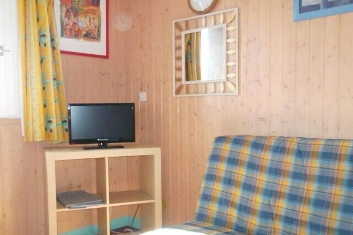Ein Zimmer mit einem karierten Sofa, einem Fernseher auf einem Holztisch, einem Bücherregal, einer Uhr und einem Spiegel an der Wand.