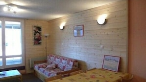 A room with a wooden wall, a sofa, a table with chairs, and a window.