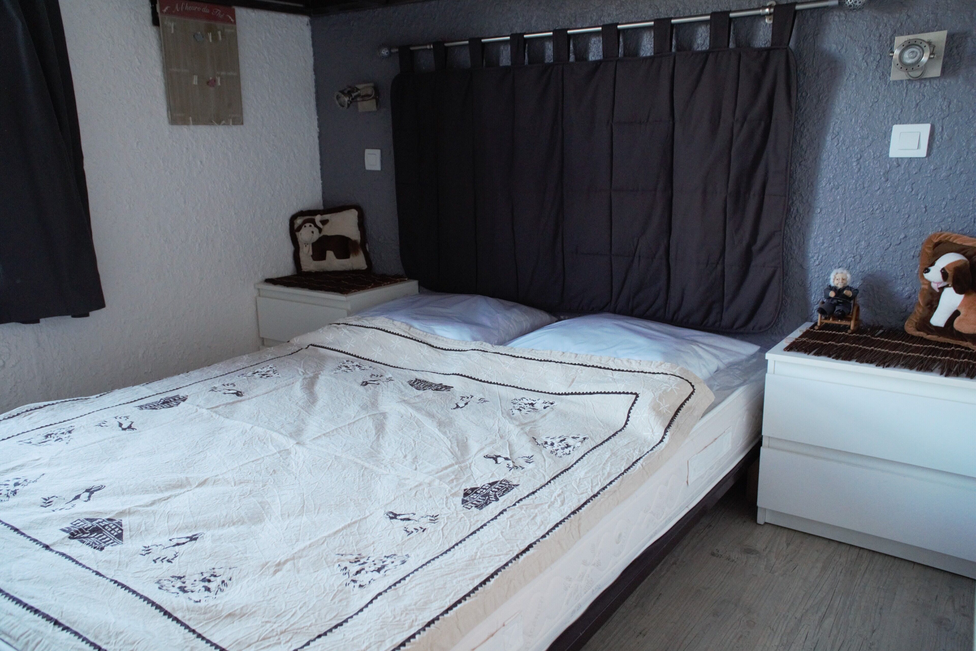 Une chambre à coucher avec un lit, une table de chevet, une commode, un rideau foncé et une horloge murale.