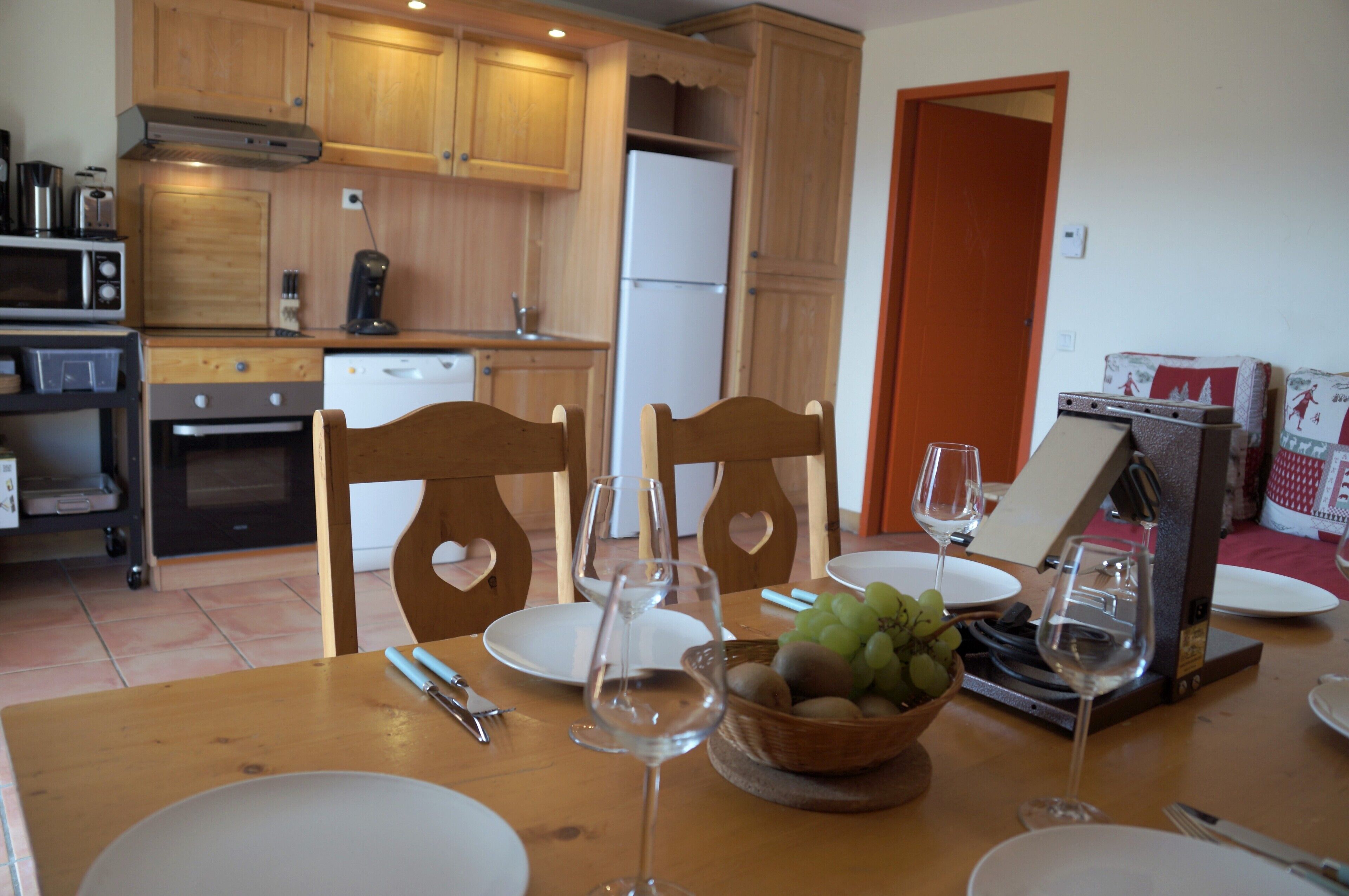 Un coin repas avec des chaises en bois, une table dressée avec des assiettes, des verres à vin et un saladier rempli de fruits.