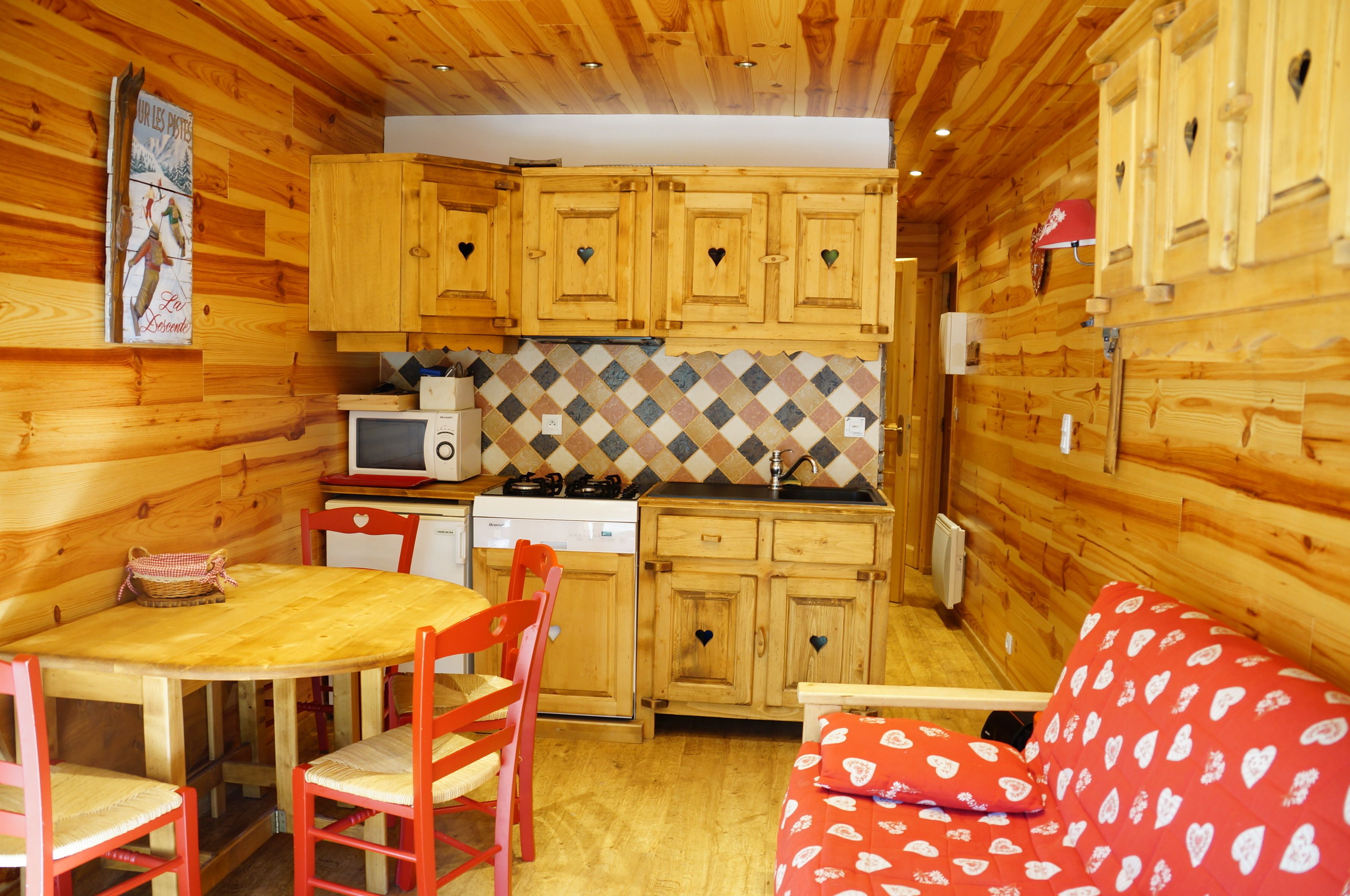 Une cuisine chaleureuse, aménagée dans le style d’un chalet, avec des meubles en bois, un four à micro-ondes, une cuisinière et un coin repas comprenant une table et des chaises.