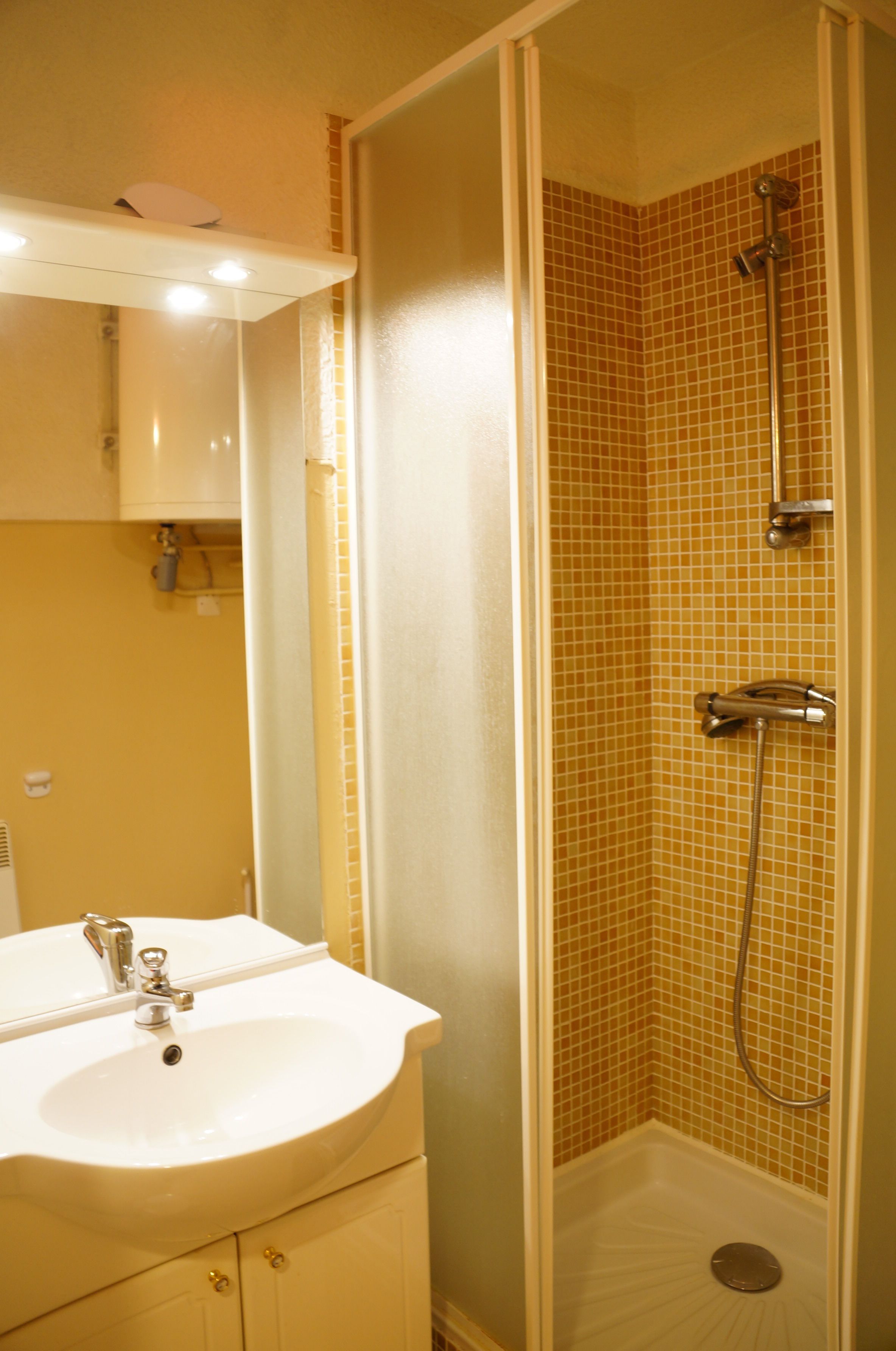 Un baño con lavamanos blanco, espejo y ducha con paredes de azulejos.