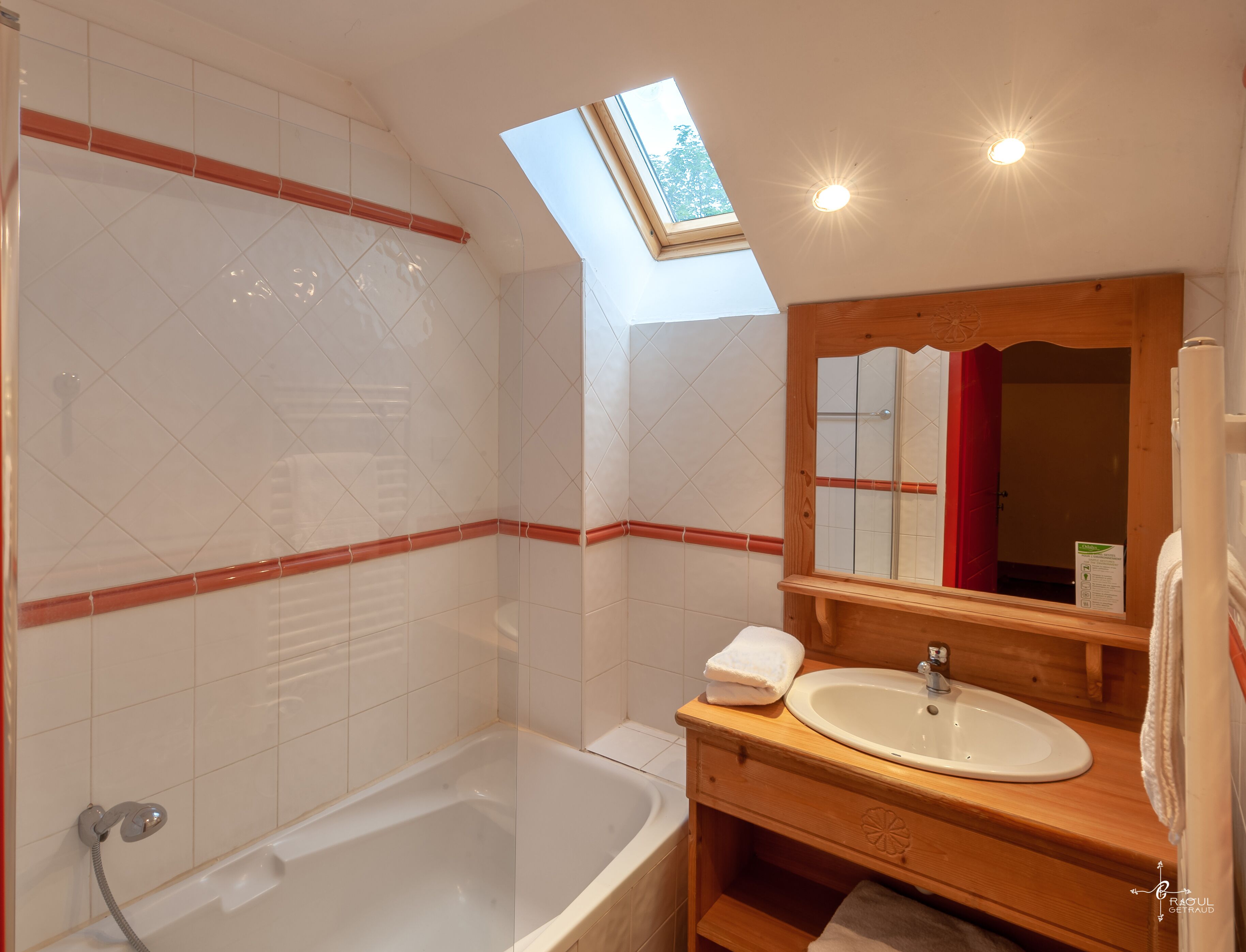 A bathroom with a skylight, a bathtub, a wooden vanity with a sink, and a mirror.