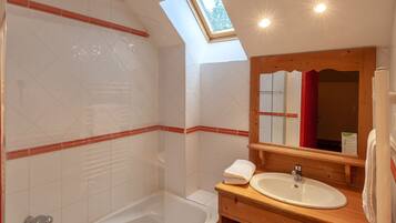 A bathroom with a skylight, a bathtub, a wooden vanity with a sink, and a mirror.