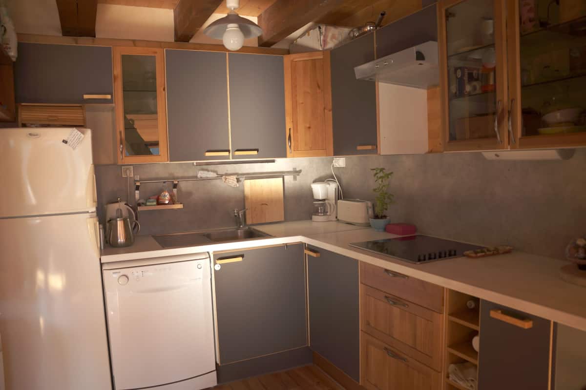 A compact kitchen with wooden cabinets, a built-in dishwasher, and a countertop with a kettle and a toaster.