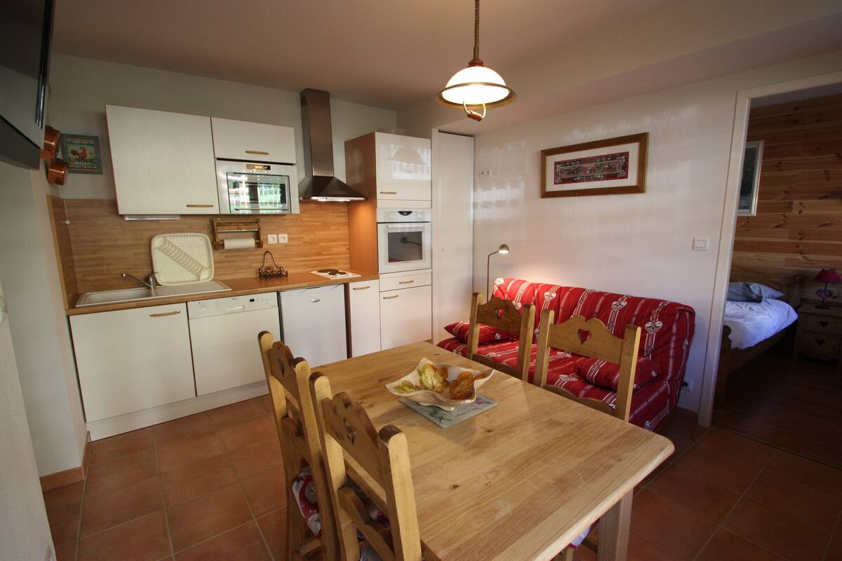 A compact kitchen with white cabinets, a wooden dining table, and a red patterned sofa.