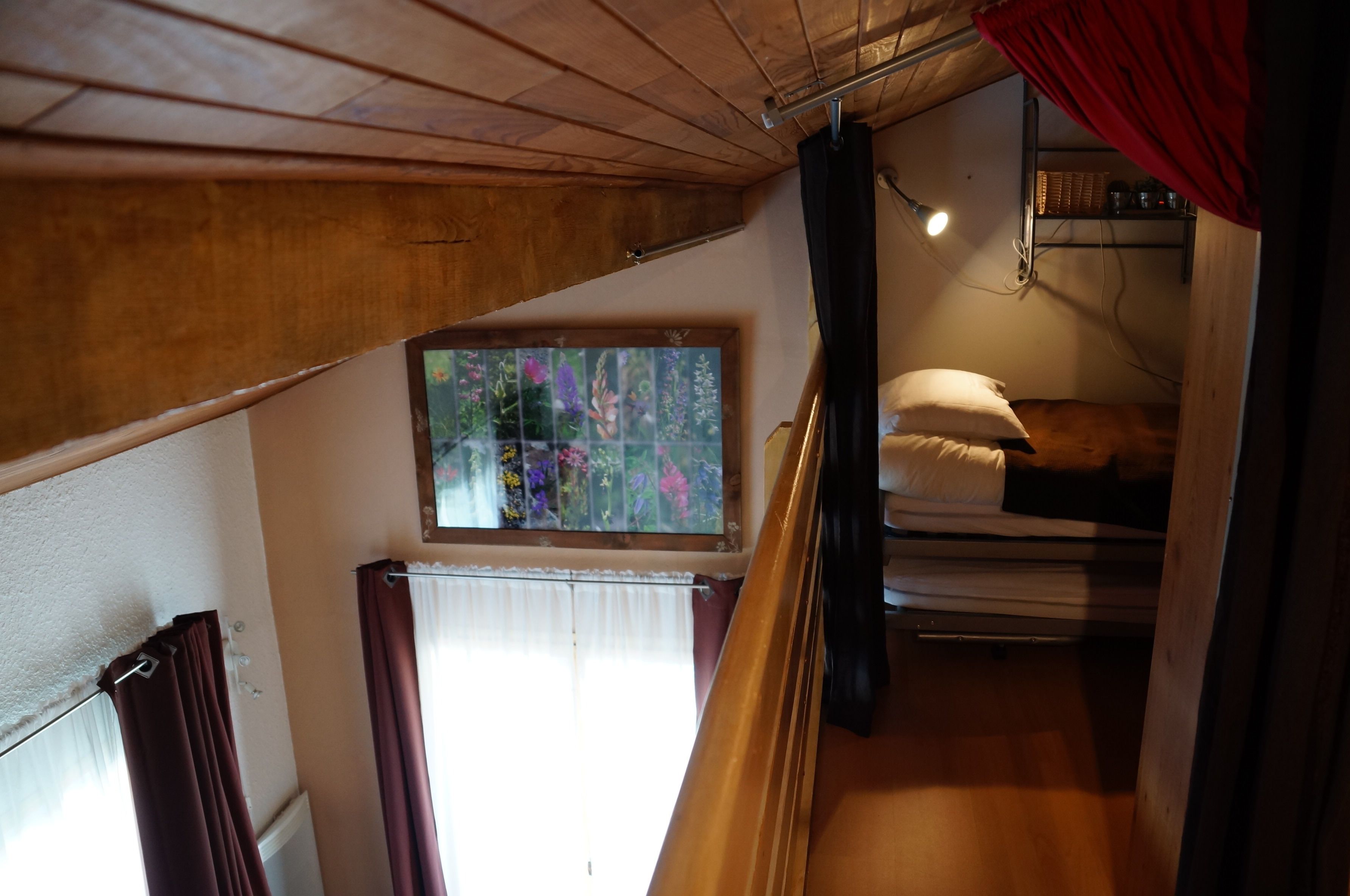 Um quarto em dormitório com uma cama de beliche, uma janela com vista para flores e uma estante com livros e um abajur.