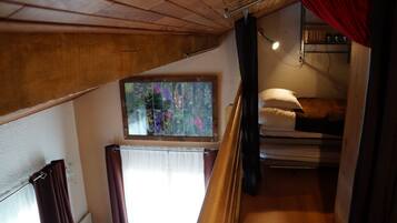 Um quarto em dormitório com uma cama de beliche, uma janela com vista para flores e uma estante com livros e um abajur.