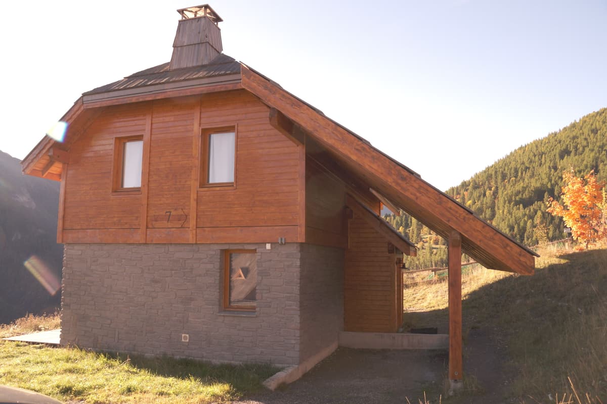 A wooden cabin with a sloped roof, a chimney, and a stone foundation.