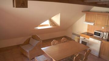 A small, cozy kitchen with a wooden table and chairs, a built-in microwave, and a small oven. There is a window providing natural light.