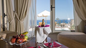 Una mesa de comedor con una cesta de frutas, un mantel blanco y vistas al océano a través de amplias ventanas.