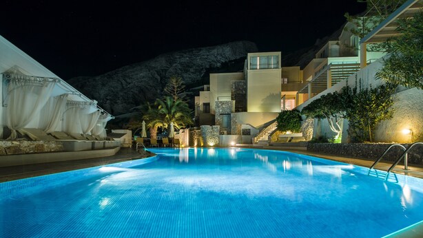 Una piscina con superficie de agua azul cristalina, rodeada por un edificio moderno con varios balcones y una escalera que lleva a un nivel superior.