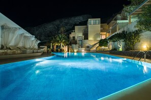 A swimming pool with a clear blue water surface, surrounded by a modern building with multiple balconies and a staircase leading to an upper level. - Hotel Antinea Suites & SPA (Santorini)