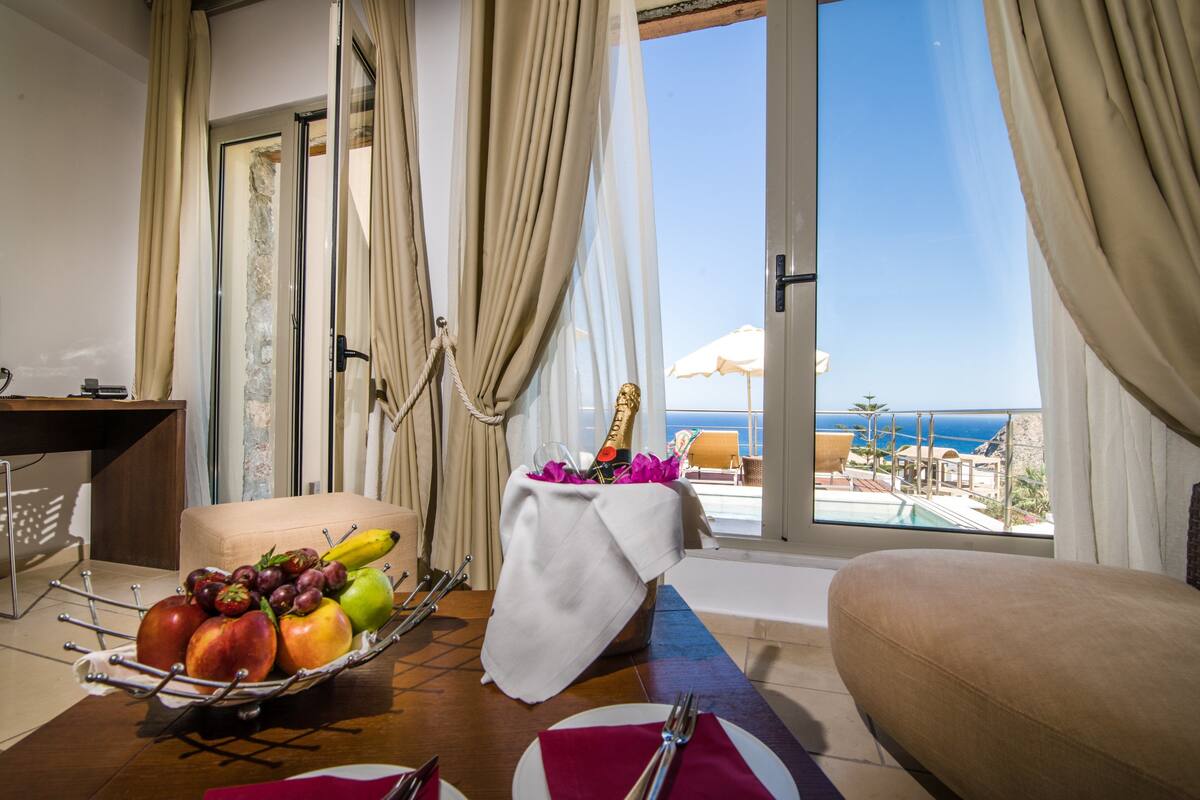 A dining area with a table set for two, a fruit basket, and a bottle of champagne.