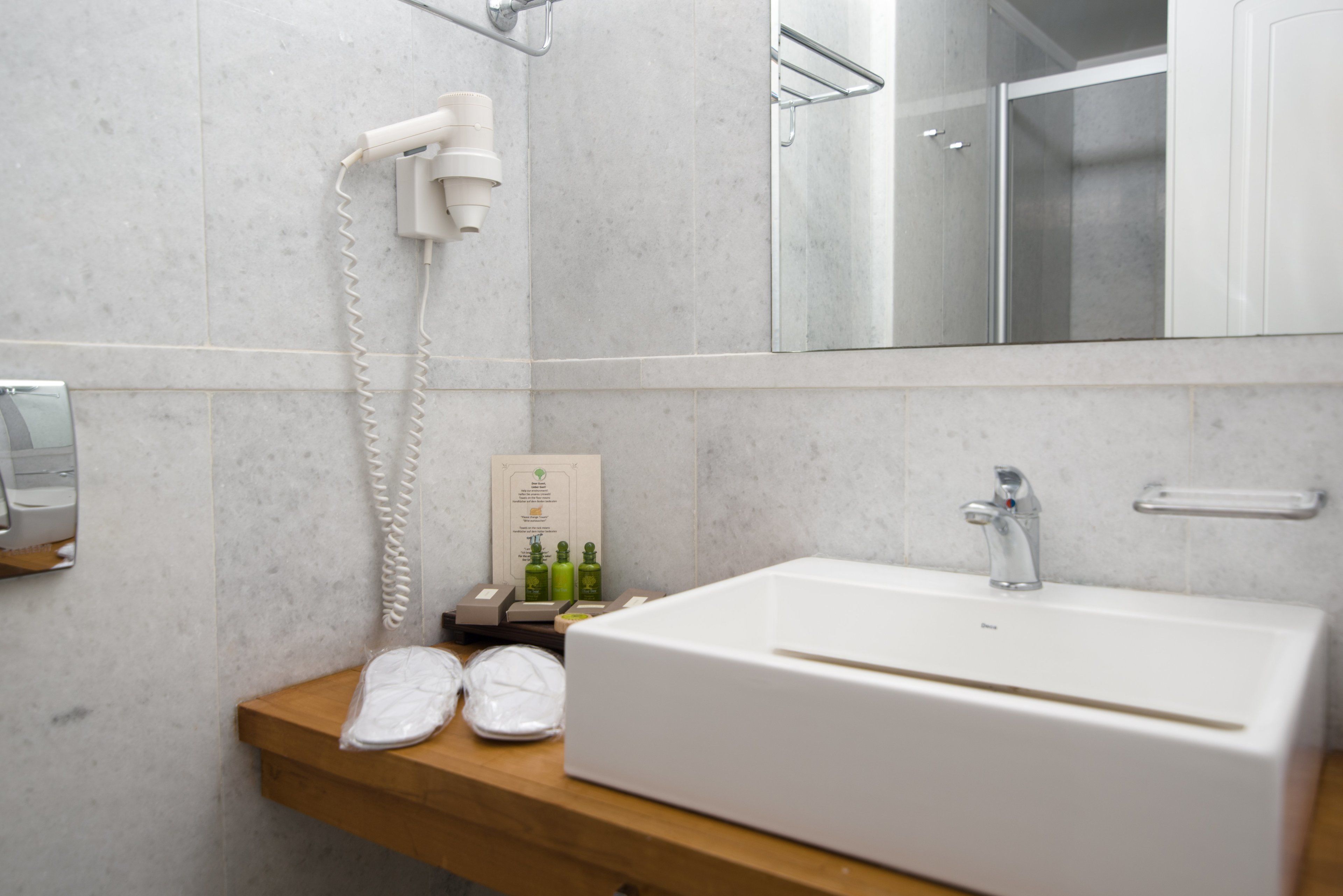Ein modernes Badezimmer mit einem weißen Waschbecken, einem Fön und Pflegeprodukten auf einem Holzregal.