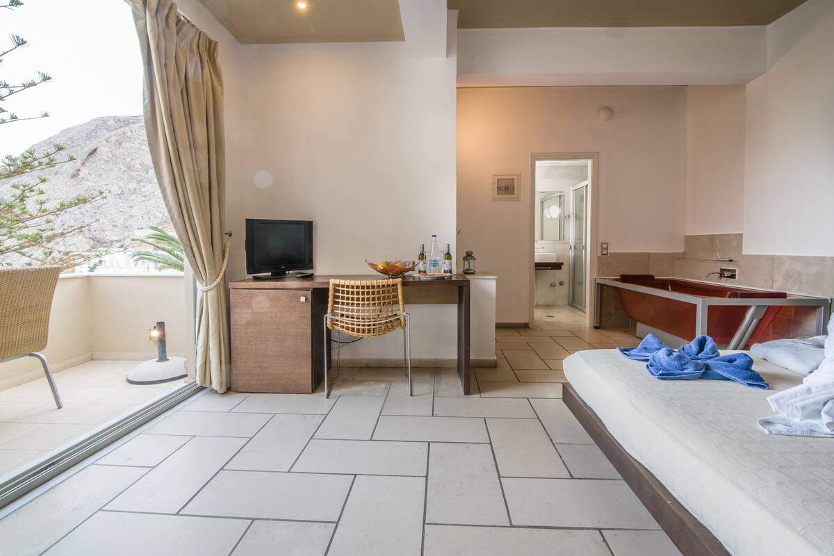 A hotel room with a bed, a desk with a chair, a television, and a bathroom with a bathtub.