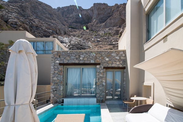Una villa moderna con piscina, paredes de piedra y vistas a montañas rocosas.