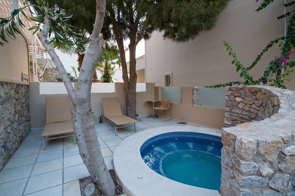 A swimming pool area with a stone wall, a lounge chair, and a small table.