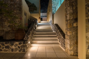 Una escalera de piedra que conduce a la entrada de un edificio, con muros de piedra a ambos lados y suelo de baldosas.