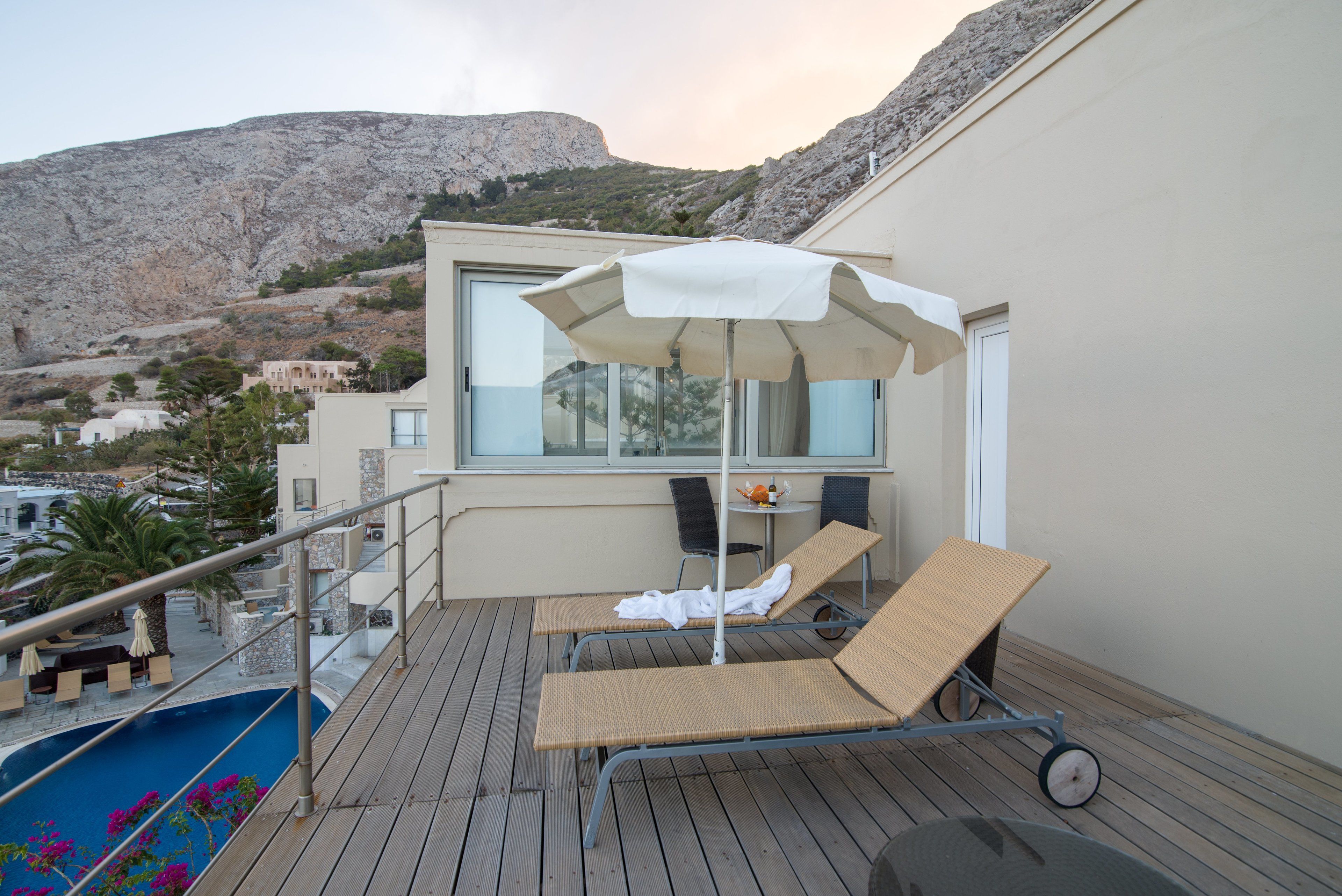 A balcony with two lounge chairs, a small table with a chair, and a large umbrella.