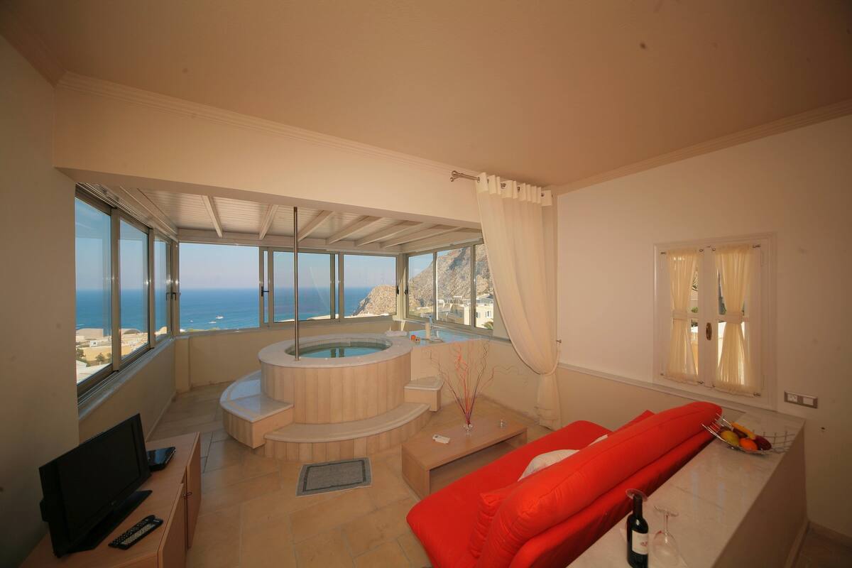A modern living room with a large window, a hot tub, and a red sofa.