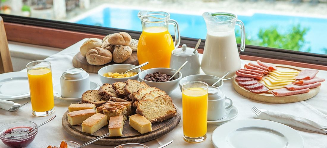 Un buffet de petit-déjeuner proposant une variété de fromages, de charcuteries et de viennoiseries, ainsi que du jus d’orange et du lait.