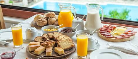 A breakfast buffet with various cheeses, meats, and pastries, along with orange juice and milk.
