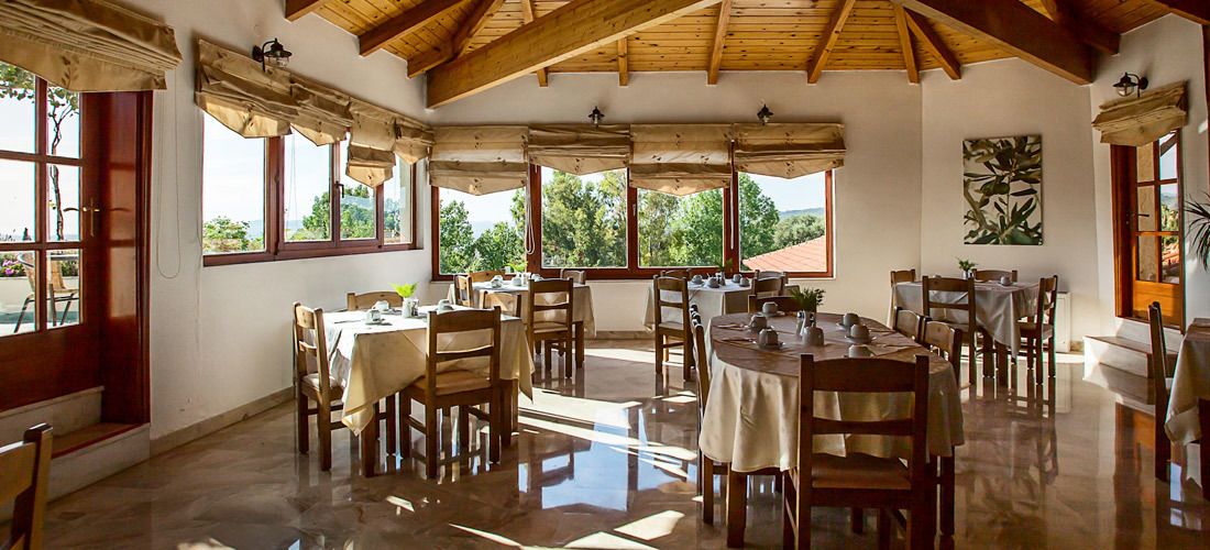 Un comedor con varias mesas y sillas, ventanas amplias con cortinas y techo de madera.