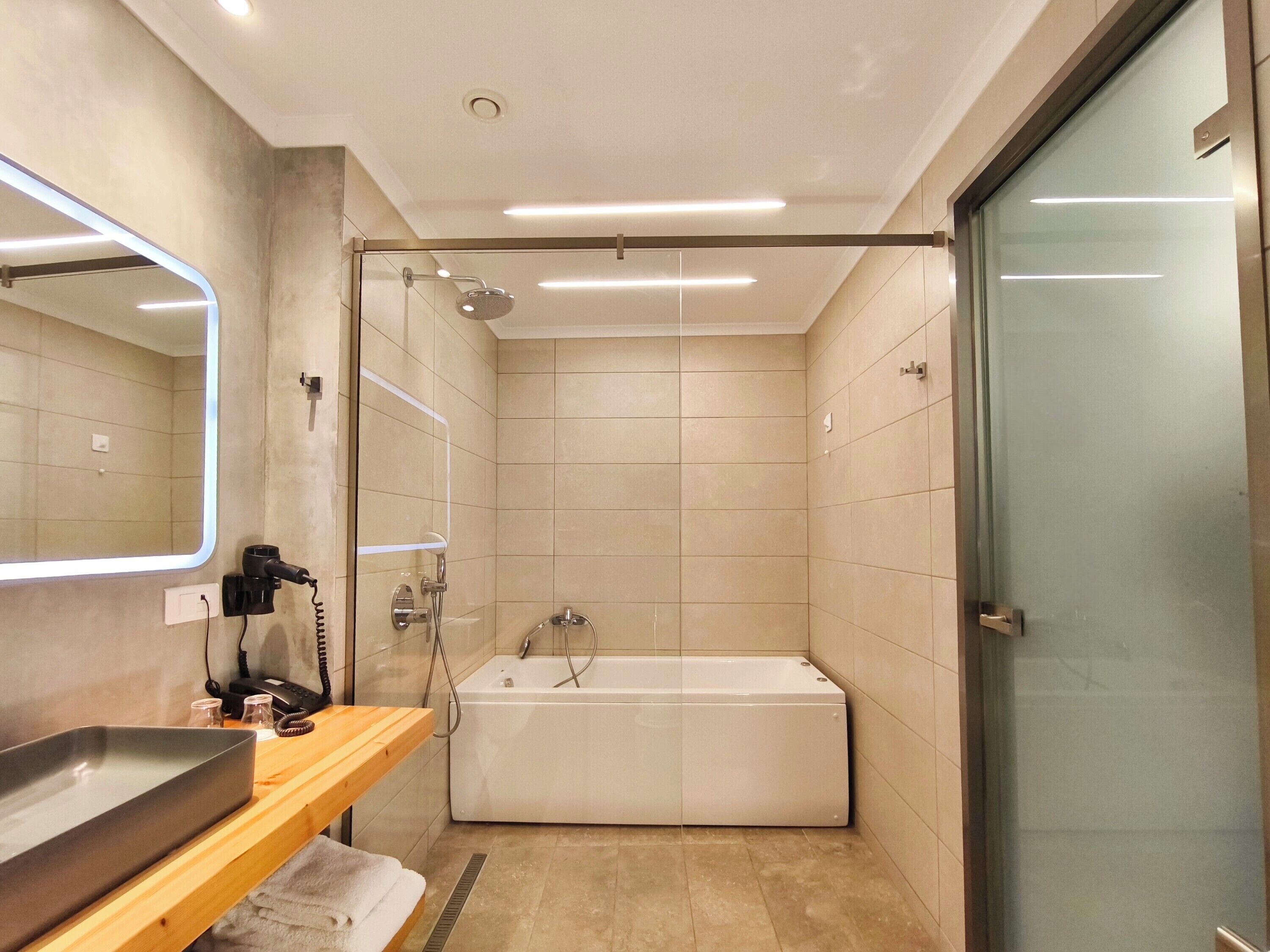 A modern bathroom with a glass shower enclosure, a white bathtub, and a wooden vanity with a mirror.