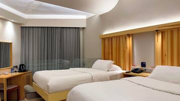 A hotel room with two beds, a desk, a chair, a coffee maker, and a telephone.