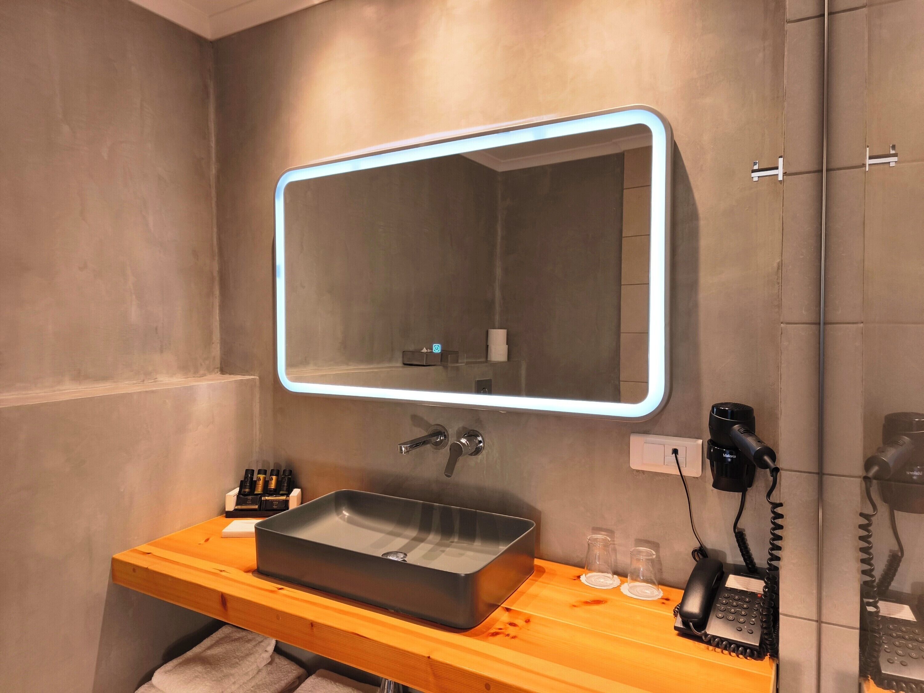 Un baño moderno con un espejo rectangular, un lavamanos integrado y un teléfono.