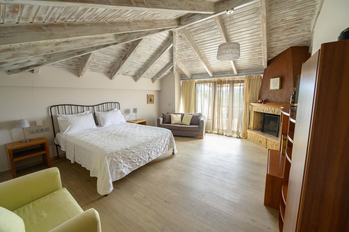 Un dormitorio amplio con una cama grande, un sofá, una chimenea y un techo de madera.