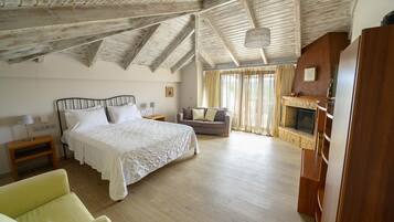 A spacious bedroom with a large bed, a sofa, a fireplace, and a wooden ceiling.