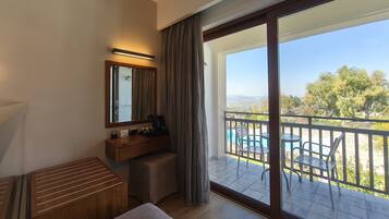 Ein Hotelzimmer mit Balkon, einem Holztisch, einem Stuhl, einem kleinen Tisch und einem großen Fenster.