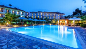 Une piscine dotée d’une terrasse en pierre, entourée de chaises longues et de parasols, avec un bâtiment visible à l’arrière-plan.