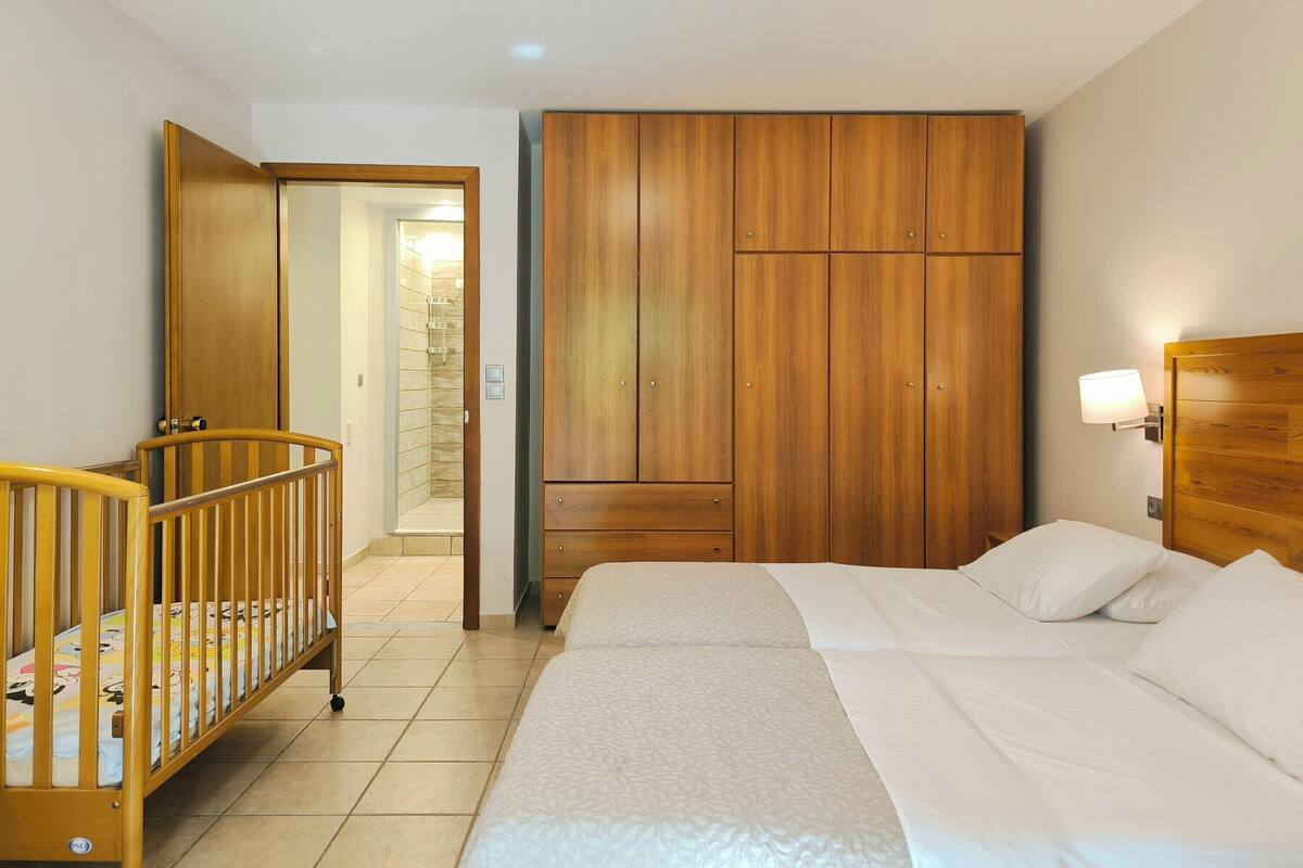 Un dormitorio con cama, cuna, armario de madera y baño con ducha.