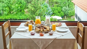 Une table de petit-déjeuner dressée avec divers aliments et boissons, une fenêtre donnant sur un paysage verdoyant.