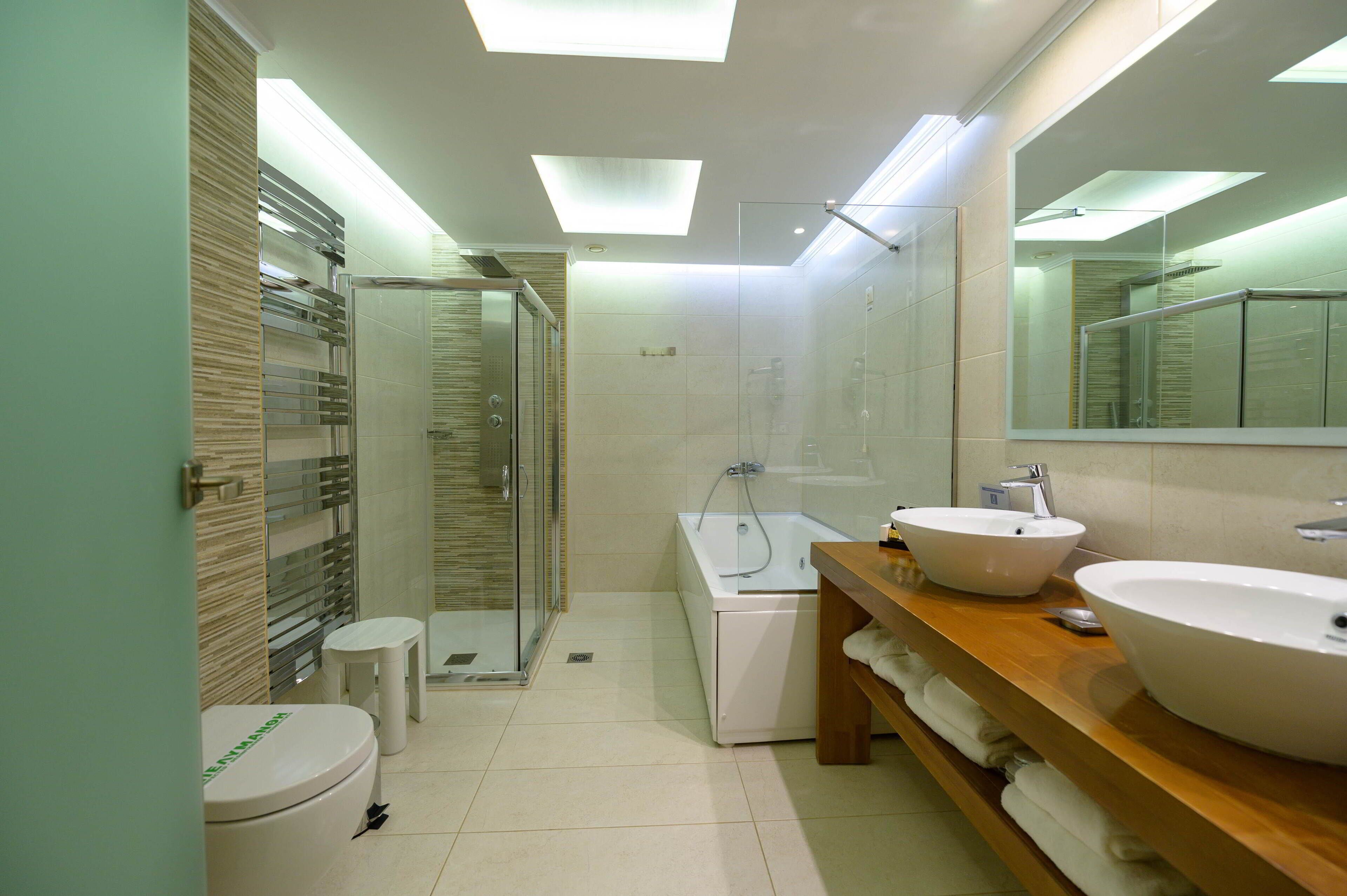 A modern bathroom with a glass-enclosed shower, a white bathtub, and two sinks on a wooden vanity.