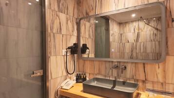 A bathroom with a marble wall, a sink with a basin, a mirror, a hairdryer, and a telephone.