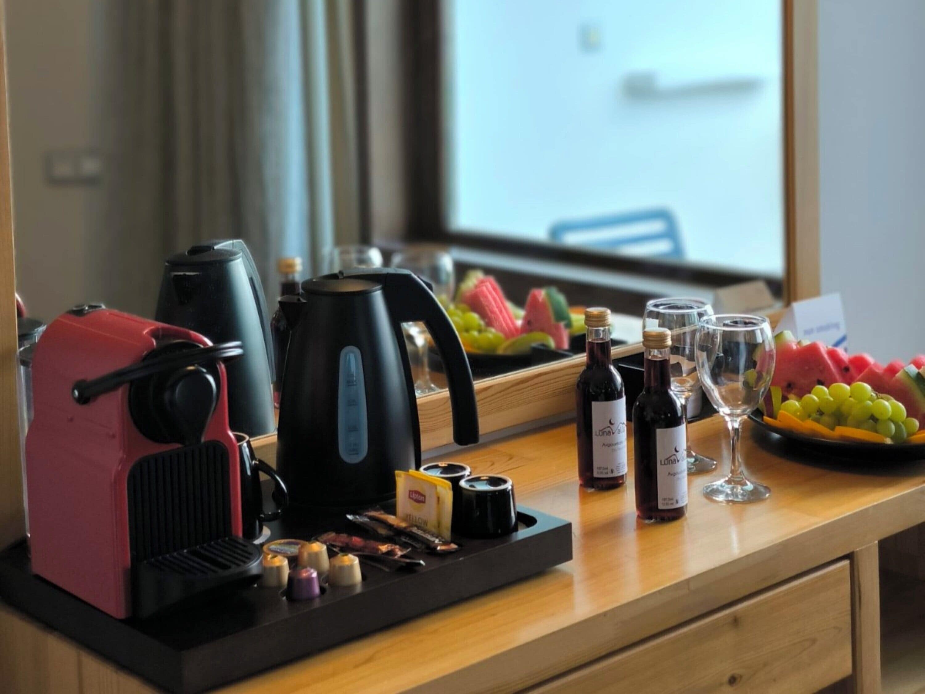 Un plan de travail de cuisine avec une machine à café, une bouilloire, des bouteilles de vin, des verres et un plateau de fruits.