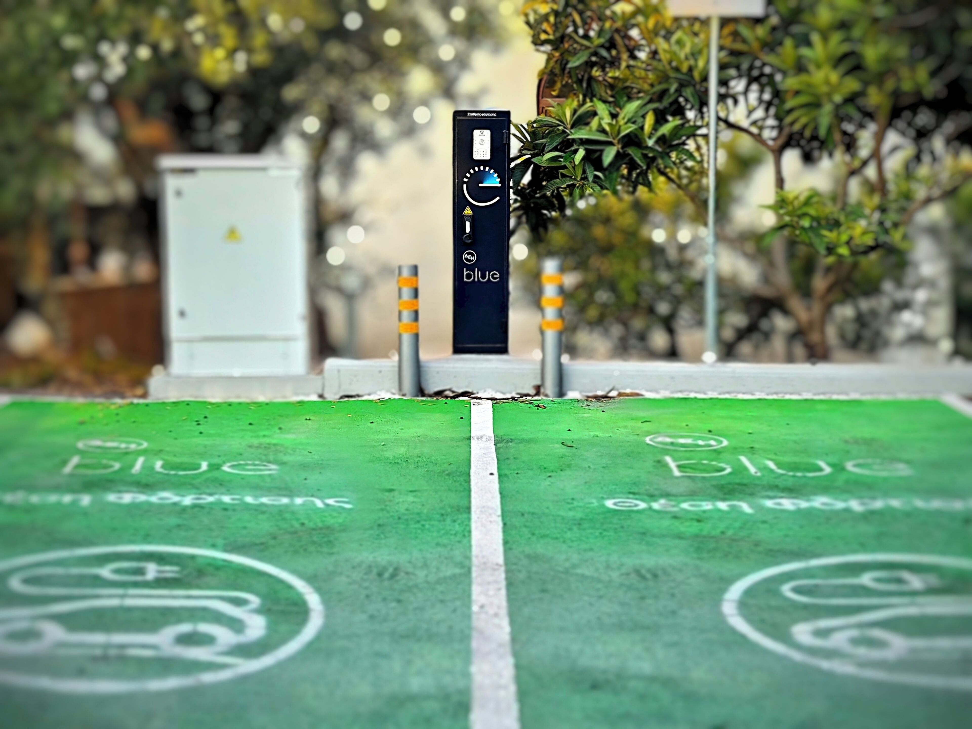 Un área de estacionamiento con marcas verdes y bolardos, una estructura blanca y vegetación al fondo.