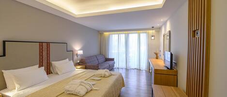 A hotel room with a large bed, a sofa, a desk with a TV, and a wooden panel on the wall.