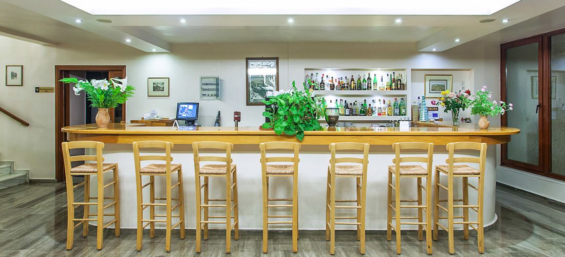 A bar area with wooden chairs and a counter, surrounded by shelves of bottles and framed pictures on the walls.