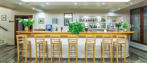 A bar area with wooden chairs and a counter, surrounded by shelves of bottles and framed pictures on the walls.
