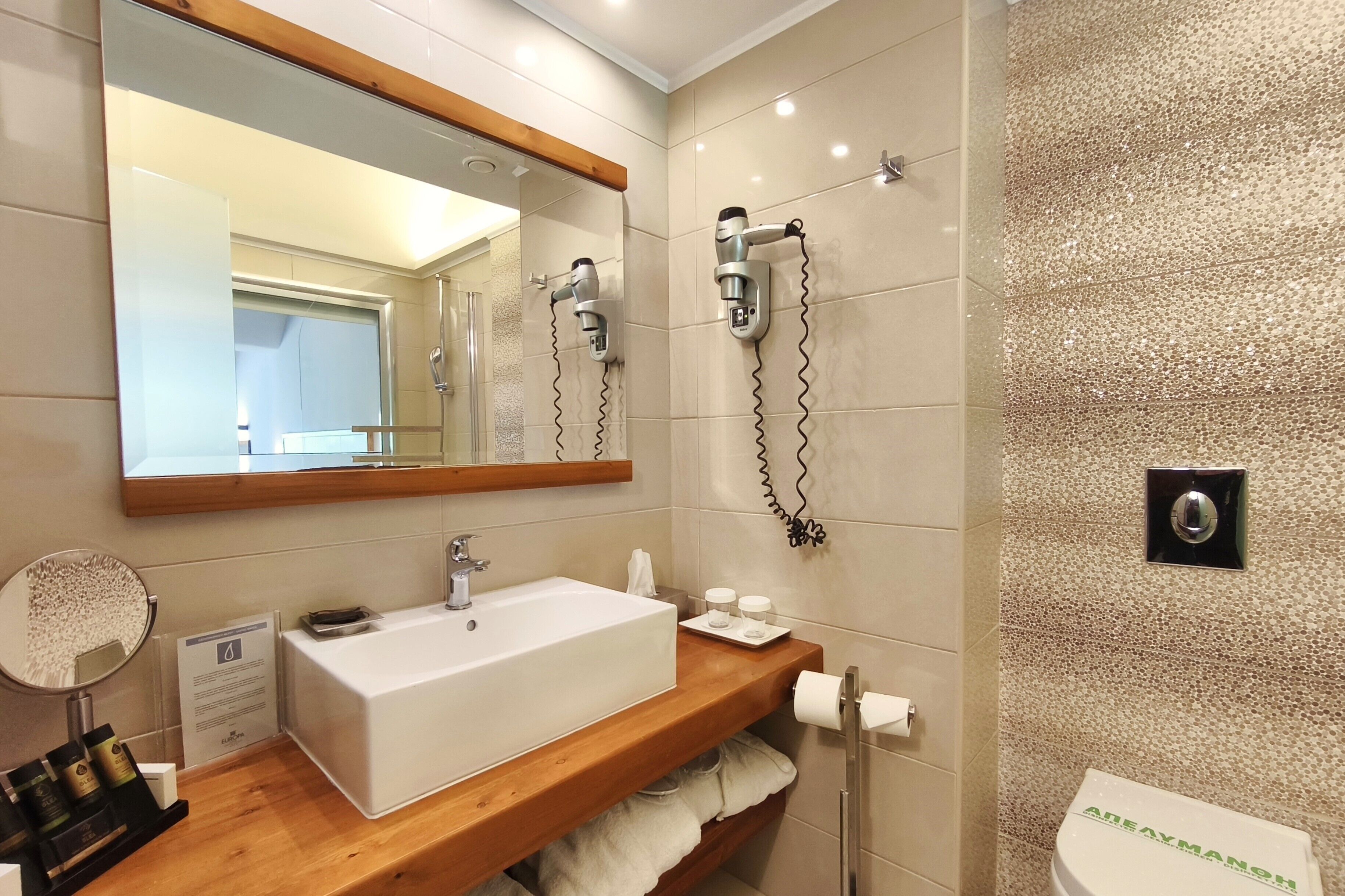 Een moderne badkamer met een grote spiegel, een wit wastafelmeubel, een handdoekhouder en een douchekop aan de muur.
