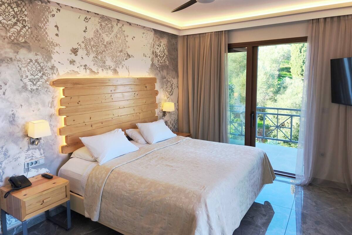Un dormitorio con cabecera de madera, cama con ropa de cama blanca, mesita de noche con teléfono, lámpara de pared y ventilador de techo.